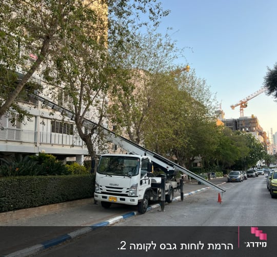 משאית מנוף חונה ברחוב ליד בניין ועצים